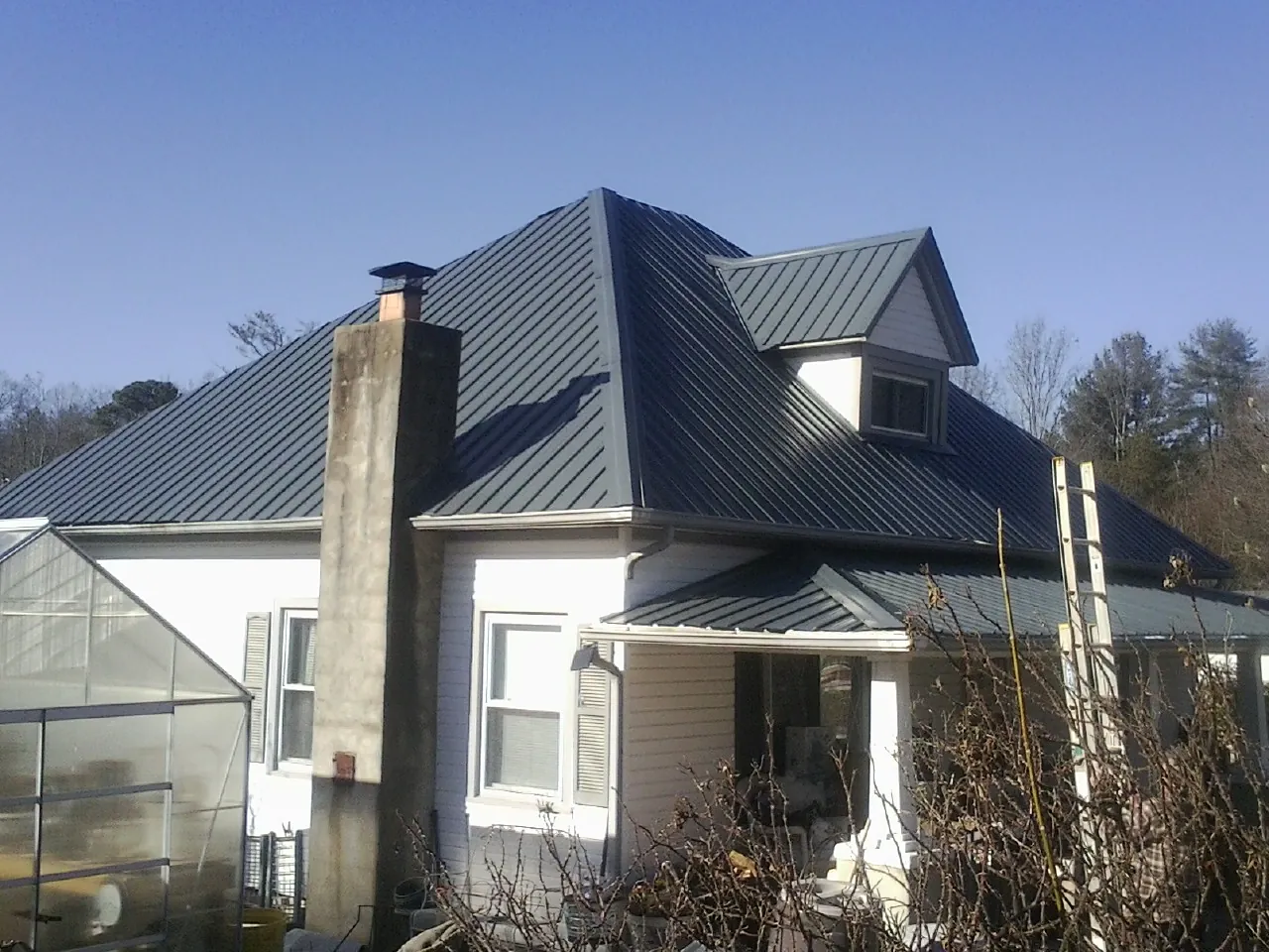 Dark blue standing seam metal roof on a white farmhouse with dormer — Slate & Tile Roof Repair by Roofing Brothers in Maidens