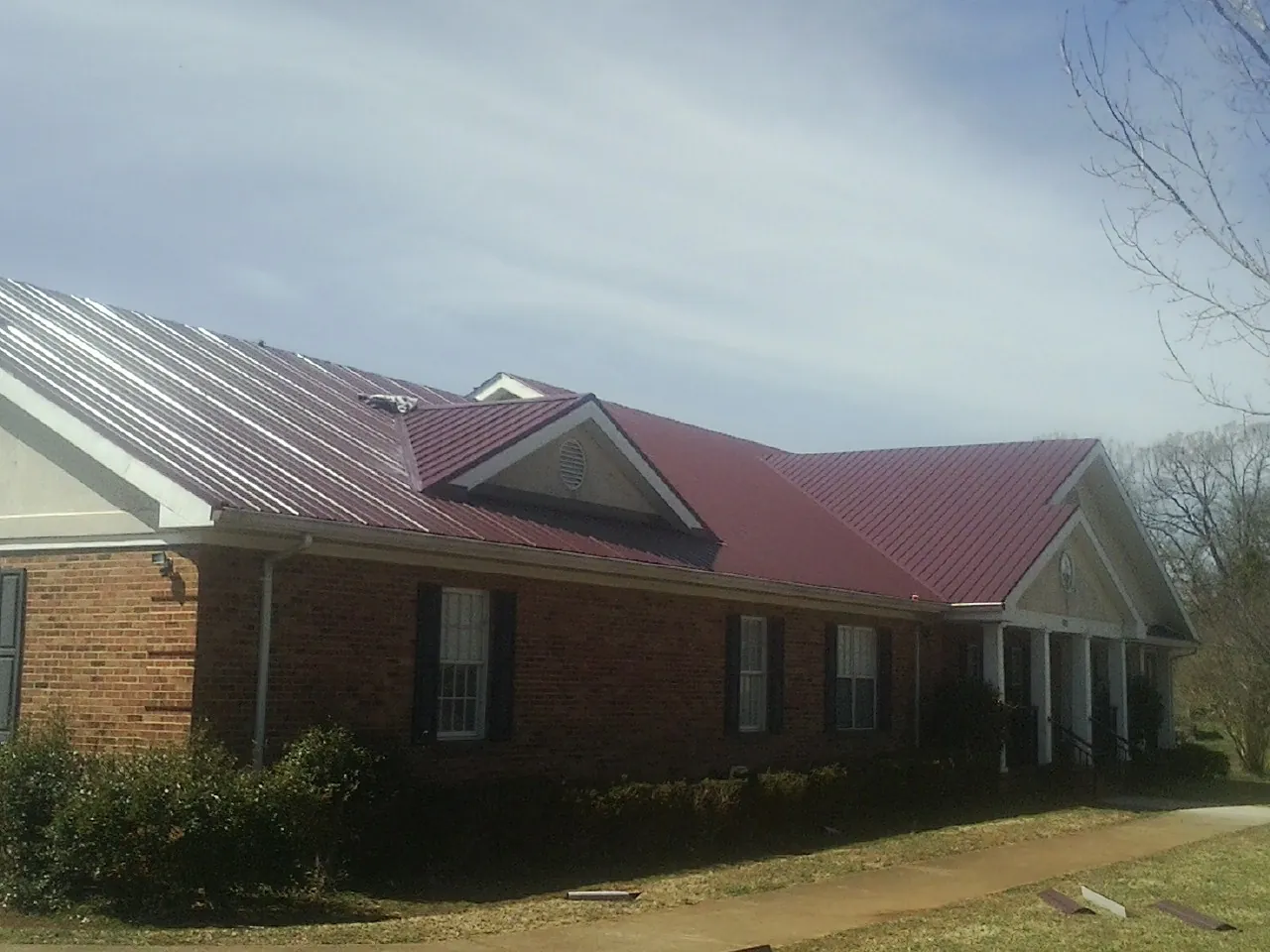 Red metal roof with gabled entries on a long brick building, from a Hail Damage Roof Repair job in Maidens