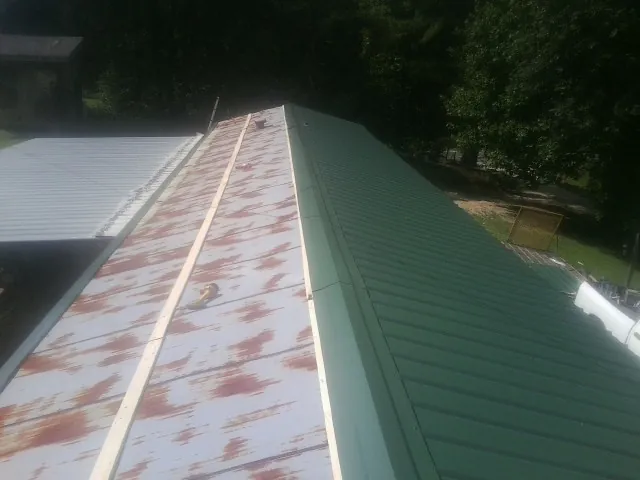 Old rusted panels beside newly installed green metal roofing — Wind Damage Roof Repair by Roofing Brothers in Maidens