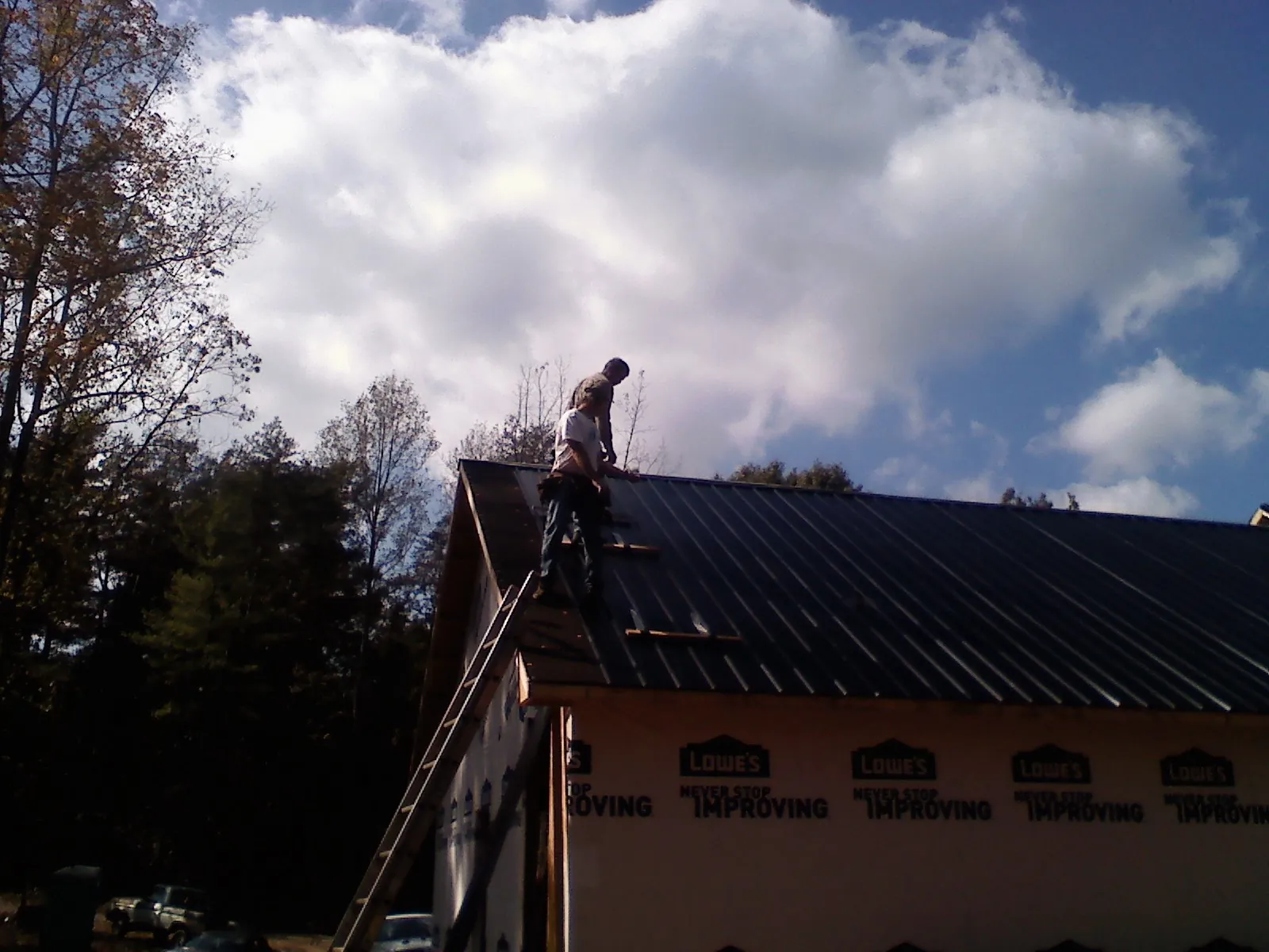 Roofer fastening dark metal panels high against a cloudy sky, from a Roof Inspection job in Maidens