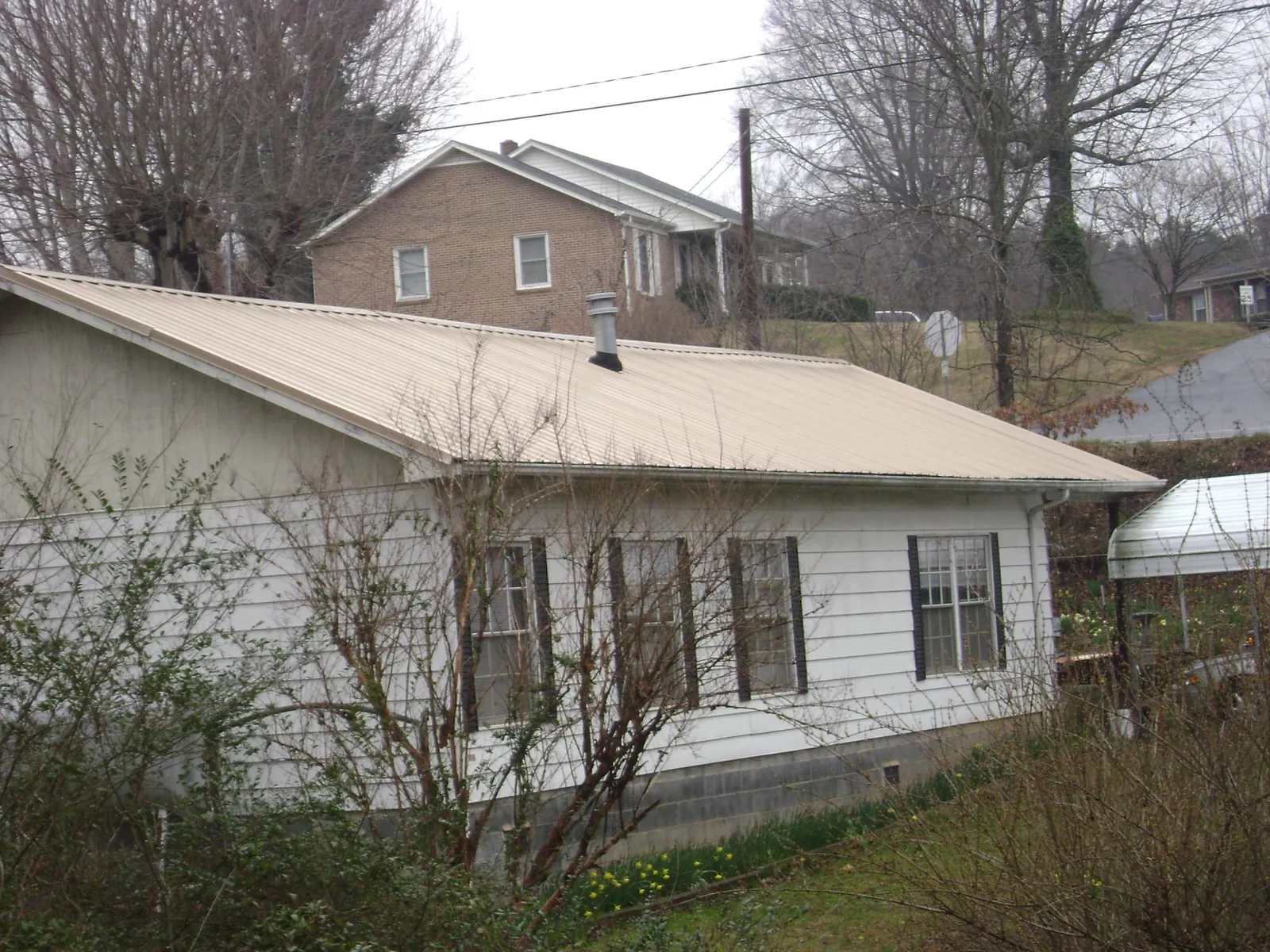 Tan metal roof on a white sided house set into a hillside — Commercial Roofing by Roofing Brothers in Maidens